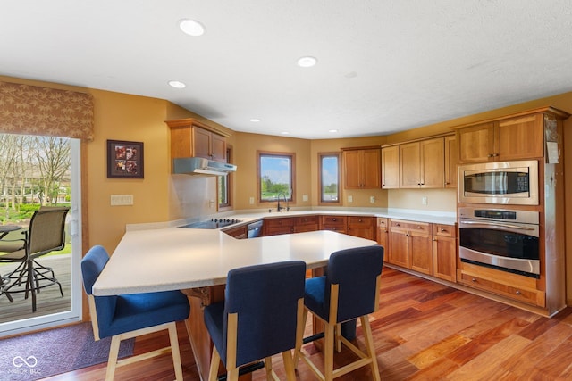kitchen with light countertops, light wood-style flooring, under cabinet range hood, and stainless steel appliances