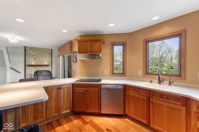 kitchen with brown cabinetry, a peninsula, under cabinet range hood, a sink, and dishwasher