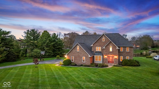 traditional home featuring a lawn, driveway, roof with shingles, and brick siding