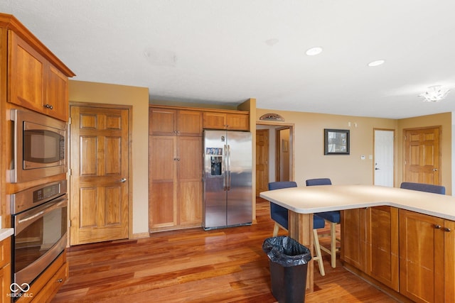 kitchen featuring brown cabinetry, light wood-style flooring, appliances with stainless steel finishes, and a breakfast bar area