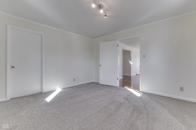 carpeted empty room with track lighting, baseboards, and ornamental molding