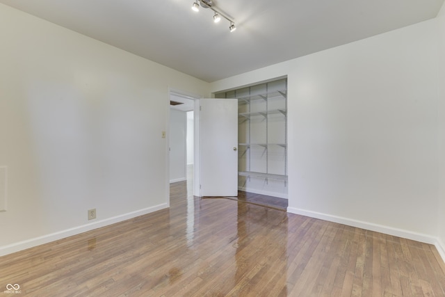 spare room featuring rail lighting, baseboards, and wood-type flooring