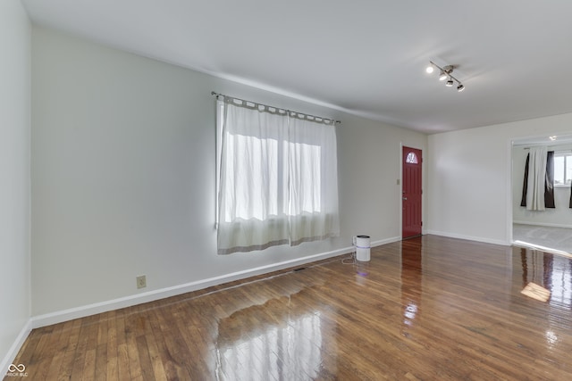 empty room featuring hardwood / wood-style floors, visible vents, and baseboards