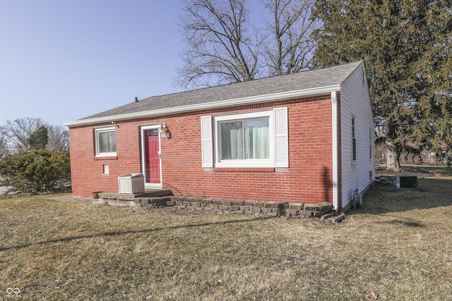 view of front of home with a front yard, brick siding, and roof with shingles