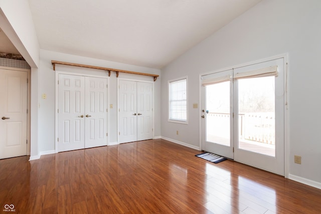 unfurnished bedroom with two closets, wood finished floors, baseboards, access to exterior, and vaulted ceiling