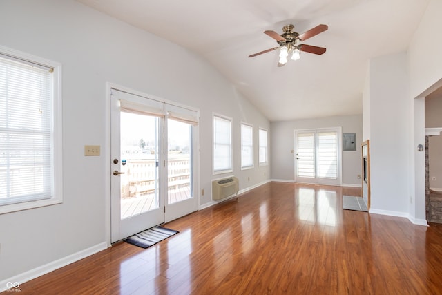 unfurnished living room with vaulted ceiling, an AC wall unit, baseboards, and wood finished floors