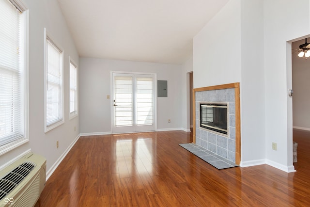 unfurnished living room with wood finished floors, a wall mounted AC, electric panel, vaulted ceiling, and a tiled fireplace