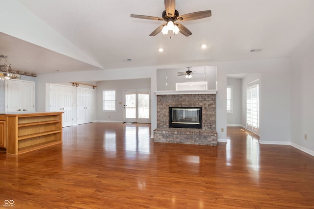 unfurnished living room with vaulted ceiling, a brick fireplace, wood finished floors, and baseboards