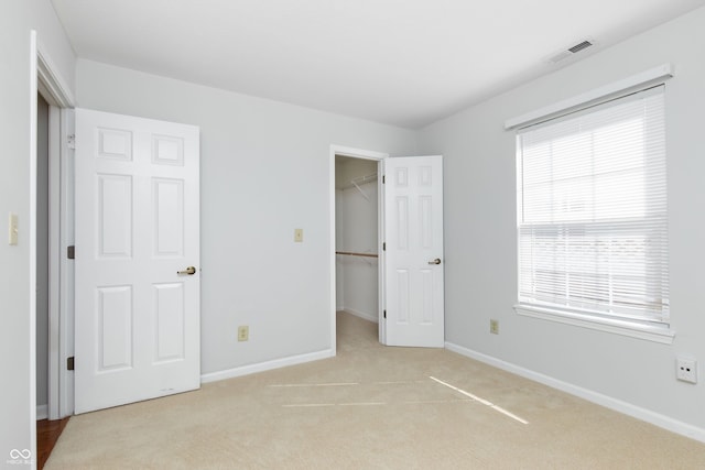 unfurnished bedroom featuring visible vents, a walk in closet, baseboards, light carpet, and a closet