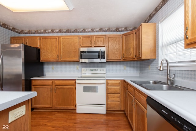 kitchen with wood finished floors, wallpapered walls, a sink, stainless steel appliances, and light countertops