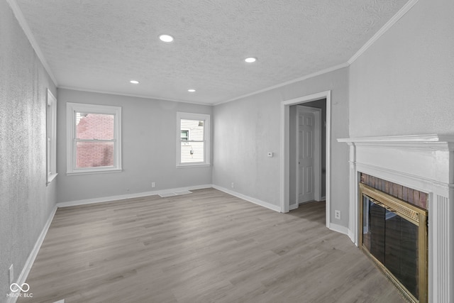 unfurnished living room with a textured ceiling, light wood-style floors, a fireplace, crown molding, and baseboards