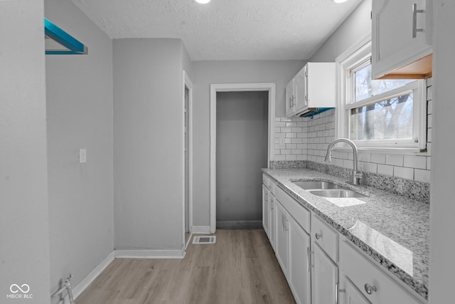 kitchen featuring light wood-type flooring, light stone counters, decorative backsplash, white cabinetry, and a sink