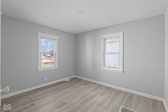 unfurnished room featuring visible vents, light wood-type flooring, and baseboards