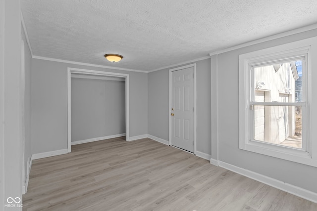 unfurnished bedroom featuring crown molding, light wood-style floors, baseboards, and a closet