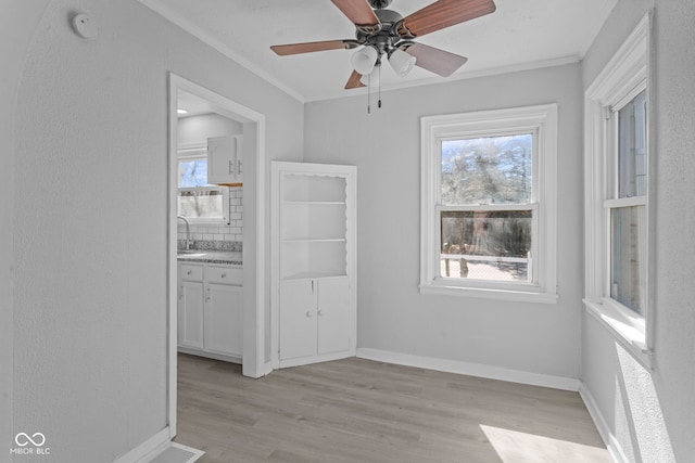 empty room with visible vents, ornamental molding, a sink, light wood-style floors, and baseboards