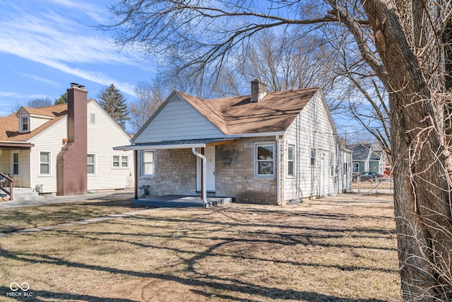 view of front facade featuring a front lawn, stone siding, a porch, a shingled roof, and a chimney