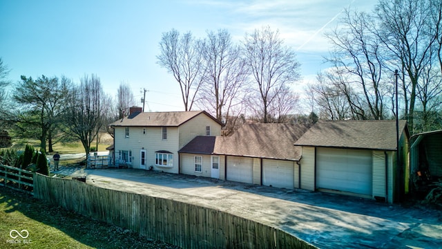 exterior space featuring an attached garage, fence, driveway, and a chimney