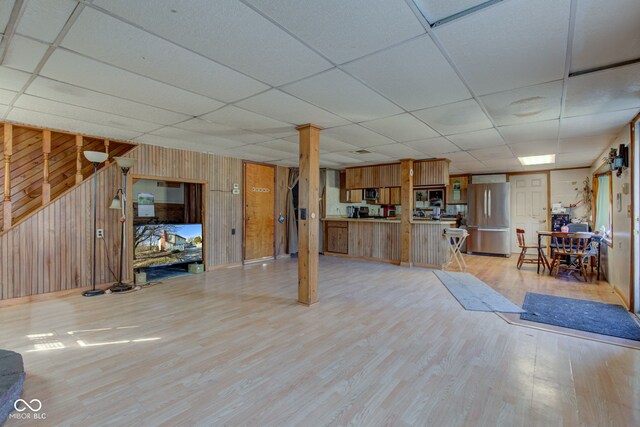 unfurnished living room featuring wooden walls, light wood-type flooring, and a drop ceiling