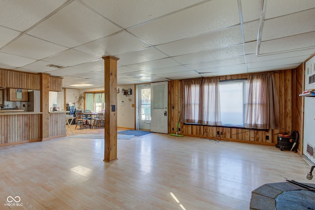 unfurnished living room featuring wood walls, light wood-type flooring, and a paneled ceiling