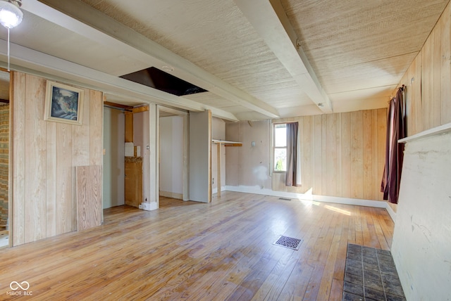 spare room with visible vents, beamed ceiling, wood-type flooring, wooden walls, and baseboards