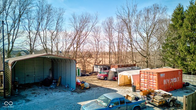 view of outdoor structure with a carport, driveway, an outdoor structure, and fence