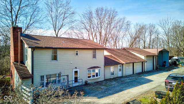 view of front of house with dirt driveway, an attached garage, a chimney, and a shingled roof