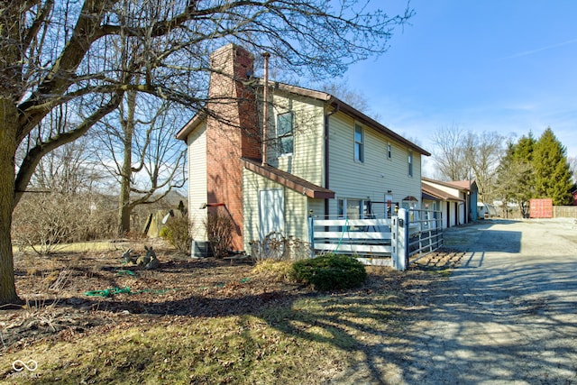 view of property exterior with driveway, a chimney, and fence