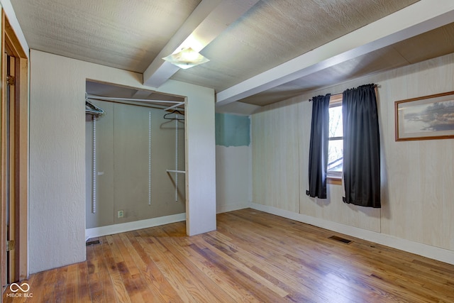 unfurnished bedroom with visible vents, beam ceiling, a closet, and hardwood / wood-style flooring