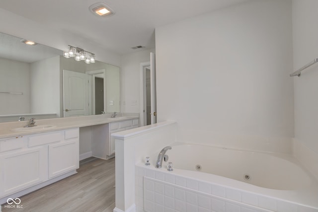 bathroom featuring visible vents, a jetted tub, double vanity, wood finished floors, and a sink