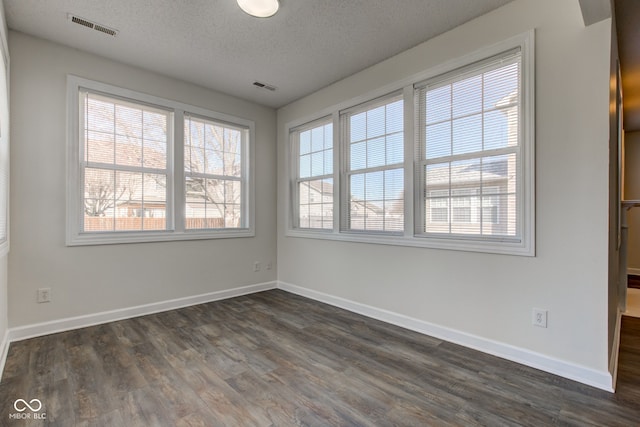 empty room featuring dark wood finished floors, baseboards, visible vents, and a textured ceiling