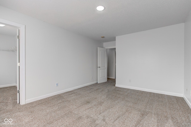 unfurnished bedroom featuring a walk in closet, baseboards, carpet floors, and a textured ceiling