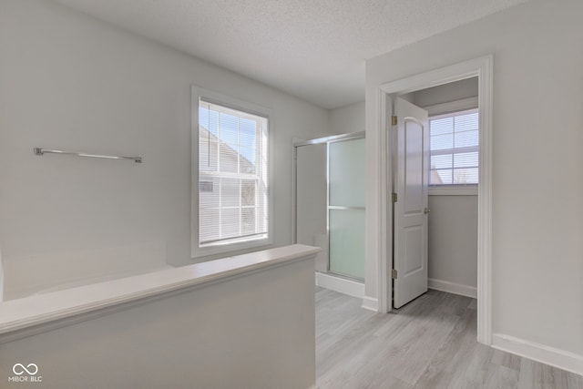 full bathroom featuring a shower stall, a textured ceiling, baseboards, and wood finished floors