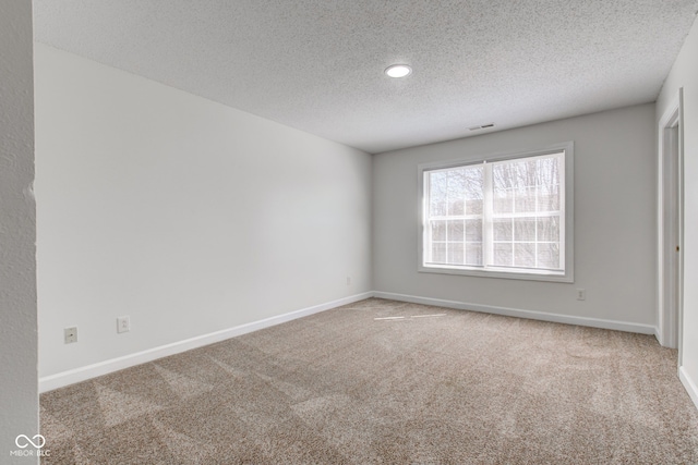 unfurnished room featuring a textured ceiling, carpet, visible vents, and baseboards