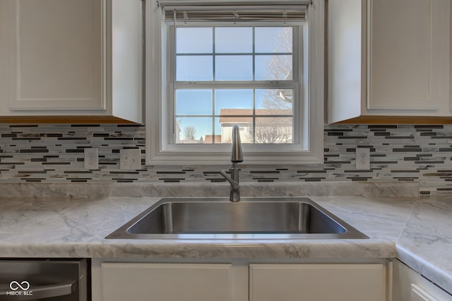 kitchen with a sink, tasteful backsplash, white cabinets, light countertops, and dishwasher