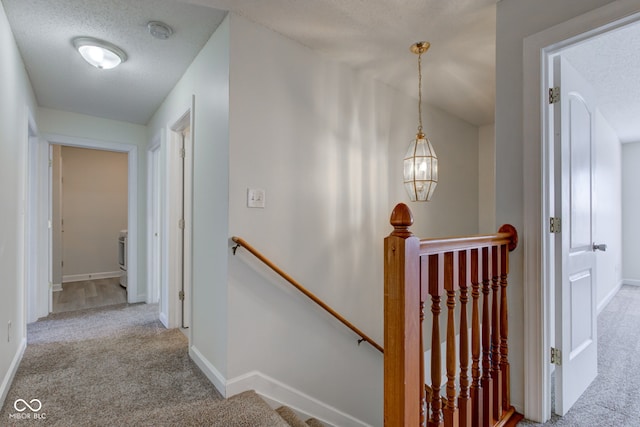 hallway featuring baseboards, an upstairs landing, a textured ceiling, and carpet flooring