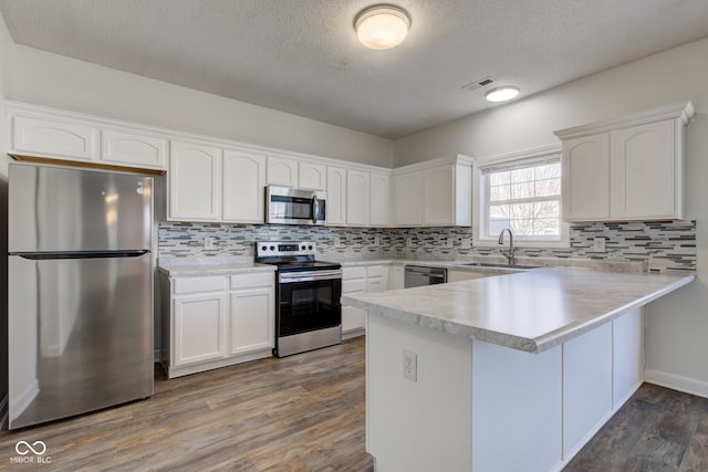 kitchen featuring visible vents, a sink, white cabinetry, stainless steel appliances, and a peninsula