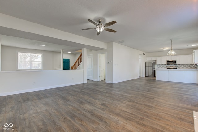 unfurnished living room with stairway, dark wood-style floors, baseboards, and ceiling fan