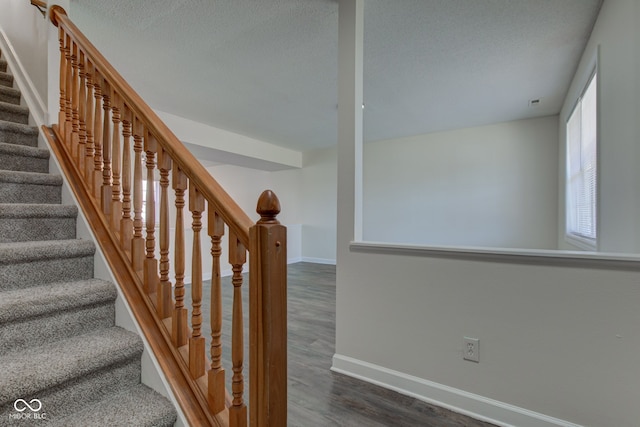 staircase featuring a textured ceiling, baseboards, and wood finished floors