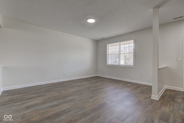 empty room featuring visible vents, baseboards, a textured ceiling, and dark wood-style floors