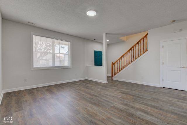 unfurnished living room with wood finished floors, visible vents, baseboards, stairs, and a textured ceiling