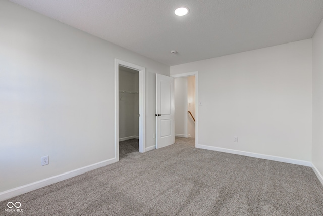 unfurnished bedroom with carpet, baseboards, recessed lighting, a closet, and a walk in closet