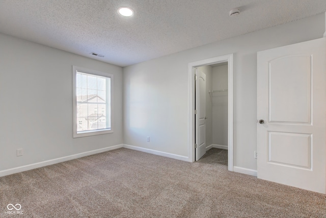 unfurnished bedroom with visible vents, a walk in closet, a textured ceiling, carpet, and baseboards