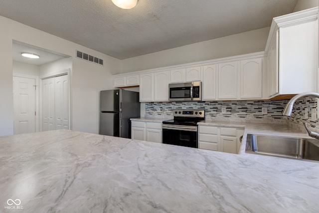 kitchen featuring visible vents, a sink, appliances with stainless steel finishes, white cabinetry, and backsplash