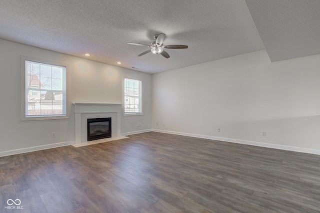 unfurnished living room featuring a fireplace with flush hearth, a textured ceiling, baseboards, ceiling fan, and dark wood-style flooring