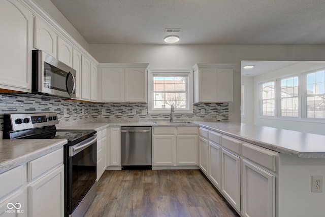 kitchen with visible vents, appliances with stainless steel finishes, a peninsula, white cabinets, and a sink