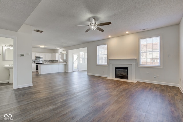 unfurnished living room featuring plenty of natural light, visible vents, dark wood-style flooring, and a fireplace with flush hearth