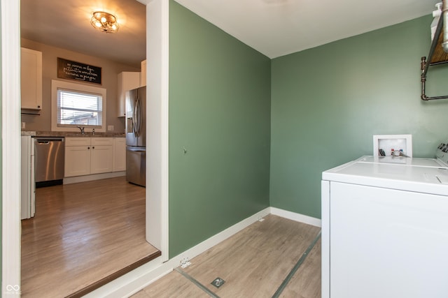 laundry area featuring independent washer and dryer, a sink, light wood finished floors, baseboards, and laundry area