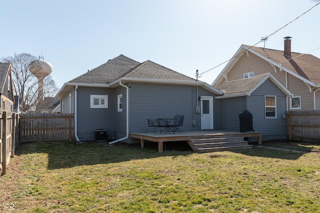 rear view of house featuring a fenced backyard, a lawn, roof with shingles, and a wooden deck