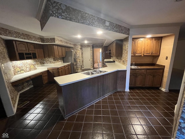 kitchen featuring a peninsula, light countertops, freestanding refrigerator, and a sink