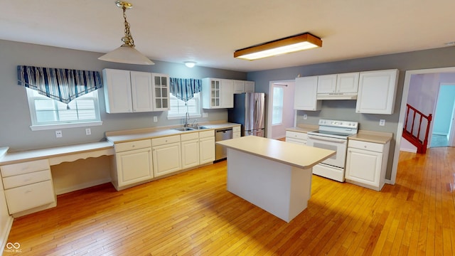 kitchen featuring under cabinet range hood, a sink, stainless steel appliances, light wood finished floors, and glass insert cabinets